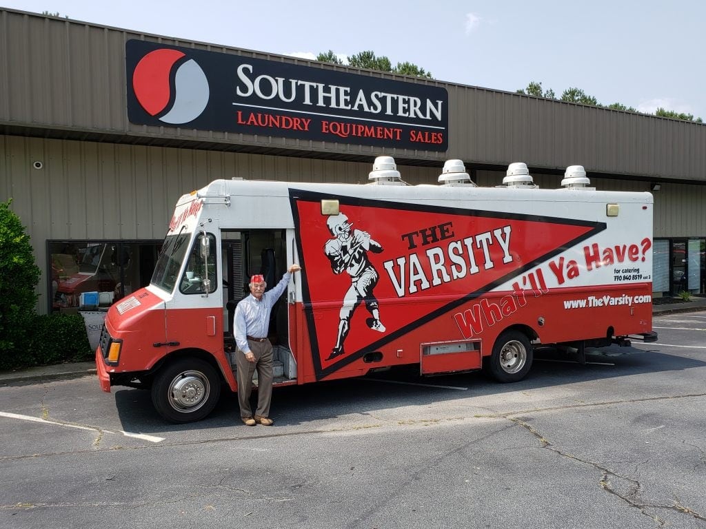 A man stands by a red and white food truck labeled The Varsity