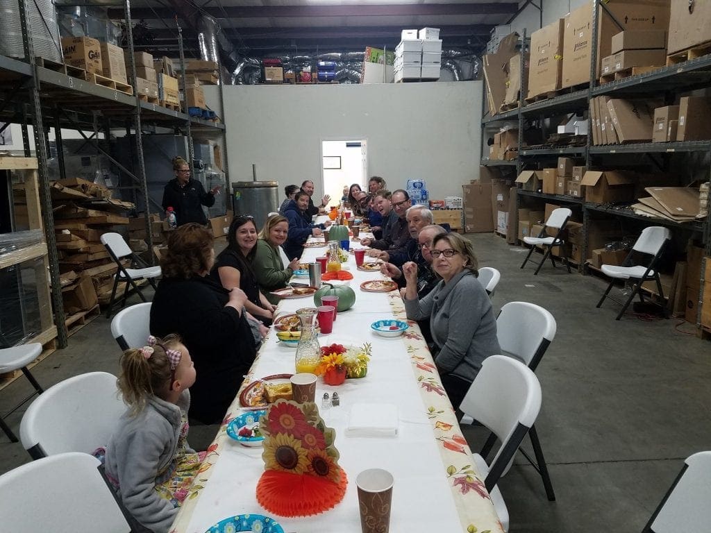 People seated at a long table in a warehouse, eating a meal