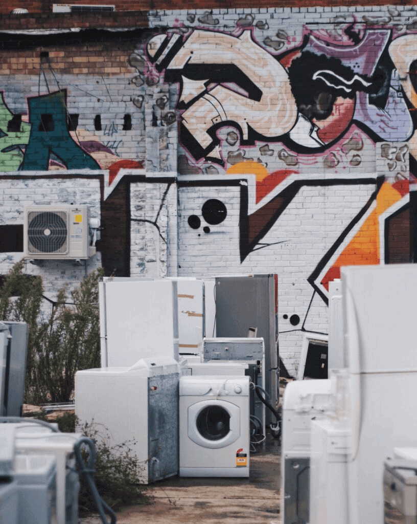 Discarded appliances against a graffiti-covered brick wall