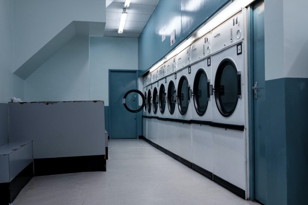 A row of white washing machines in a laundromat, with a blue door and walls