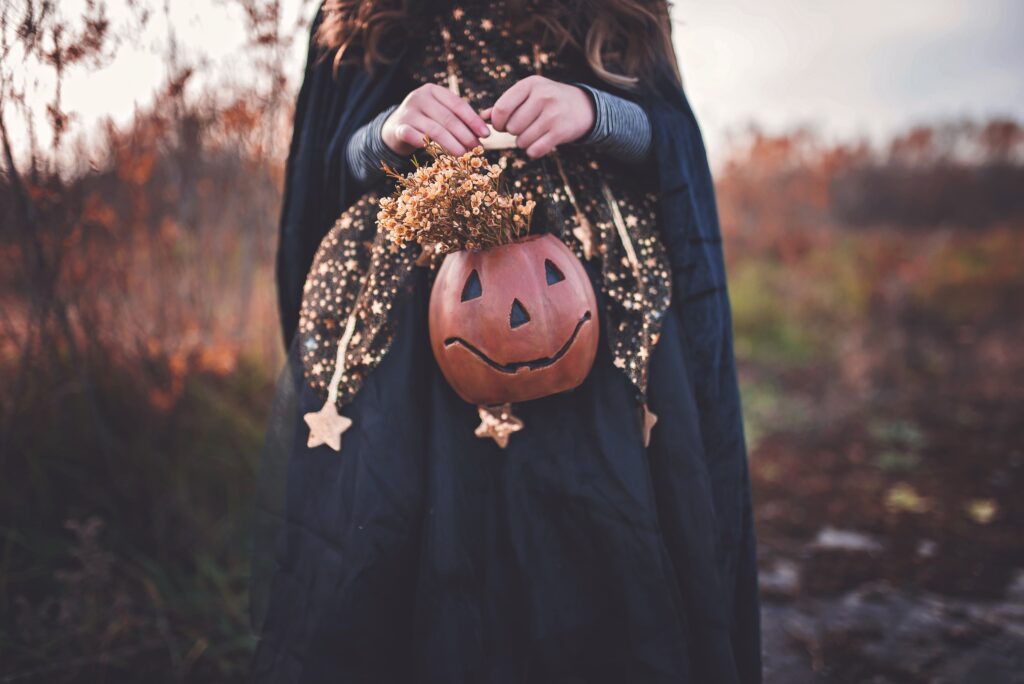 Child in black cloak holding pumpkin-shaped basket with dried flowers and star decorations