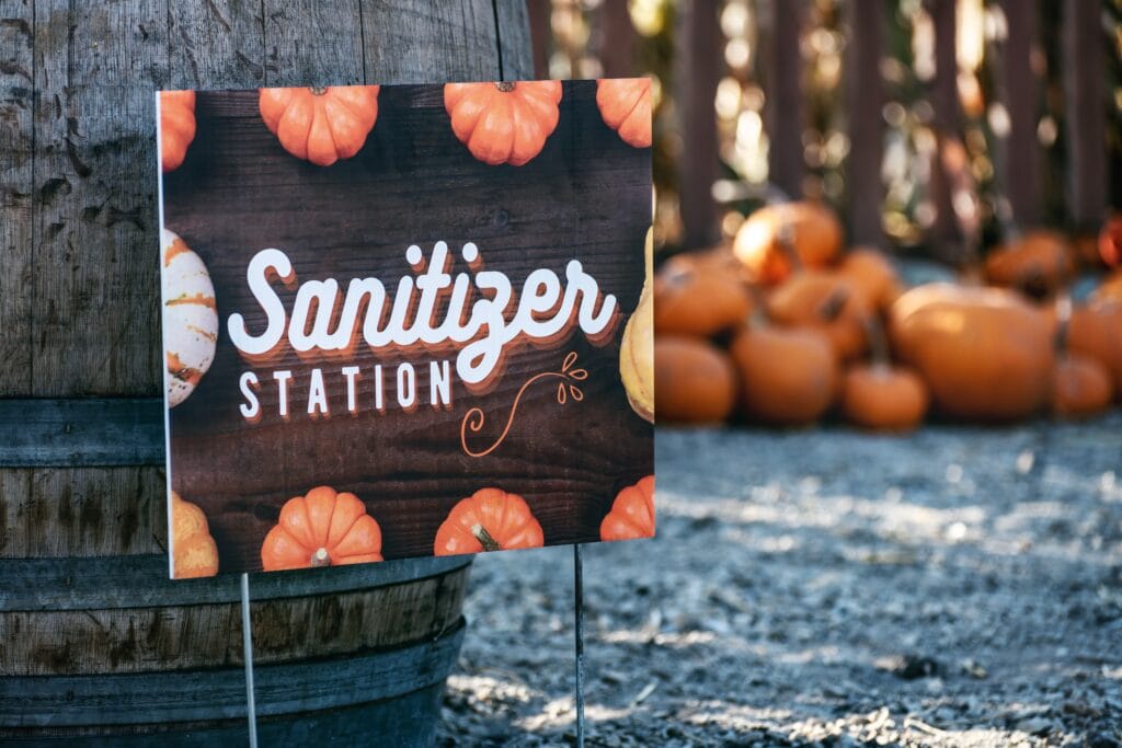 Sanitizer Station sign with pumpkins border, pumpkin patch in the blurred background