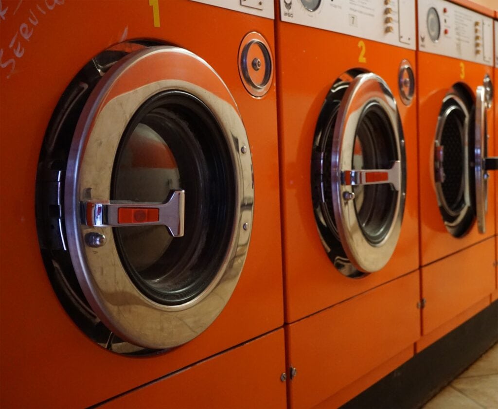 A row of orange commercial washing machines with open, silver doors
