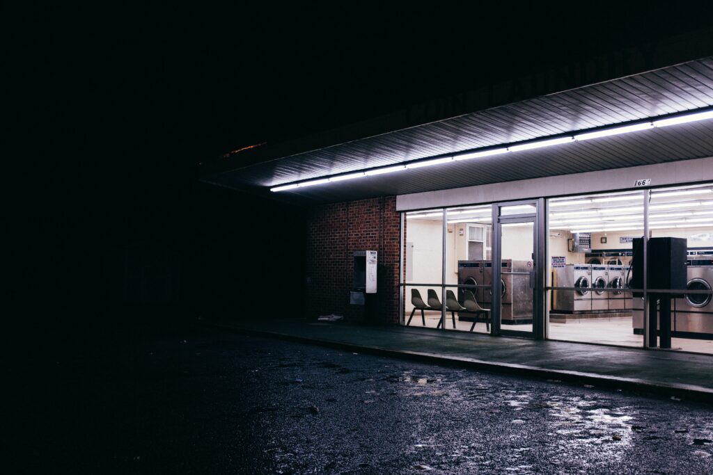 A dimly lit laundromat at night, with rows of washing machines inside