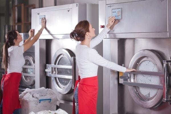 Two women operating industrial washing machines in a laundromat
