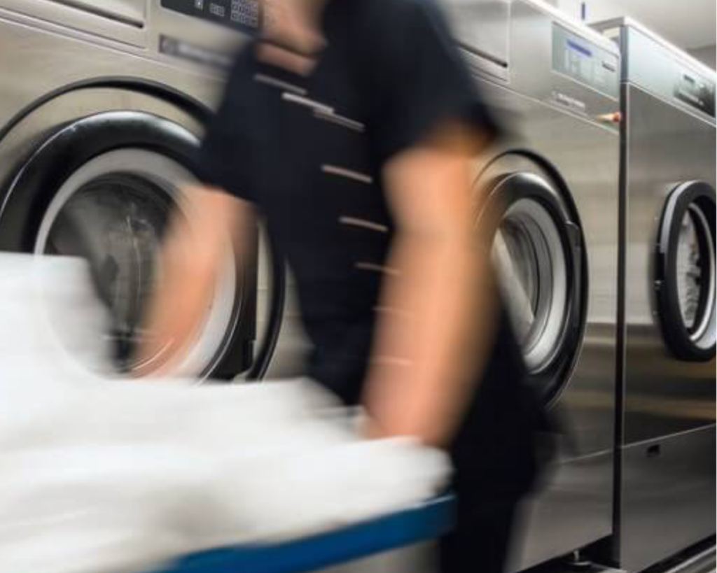 Busy laundromat worker moving linens near machines maintained by SELaundry Madison washer and dryer repair technicians.