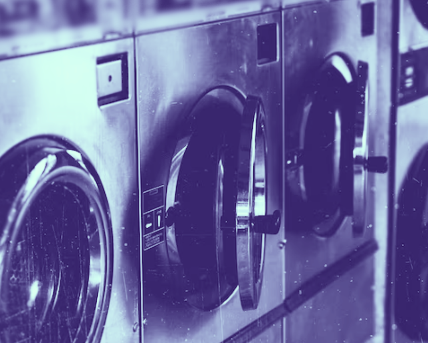 Row of stainless steel front-load washers lined up in a commercial laundry room