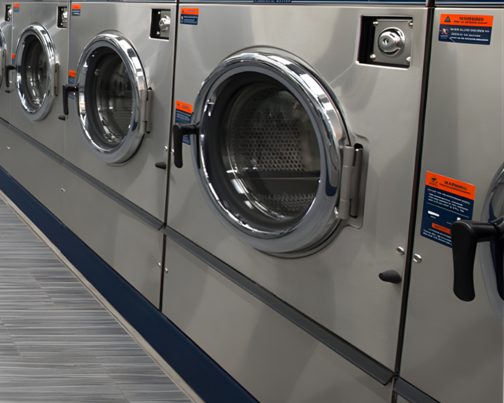 Row of commercial front-load washers with stainless steel doors, installed in a shared laundry room serving Morrisville, NC properties.