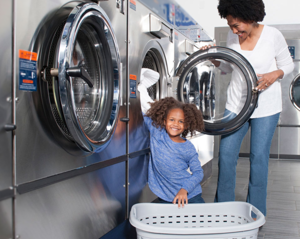 Family doing laundry together in a shared apartment laundry space with front-load commercial washers.