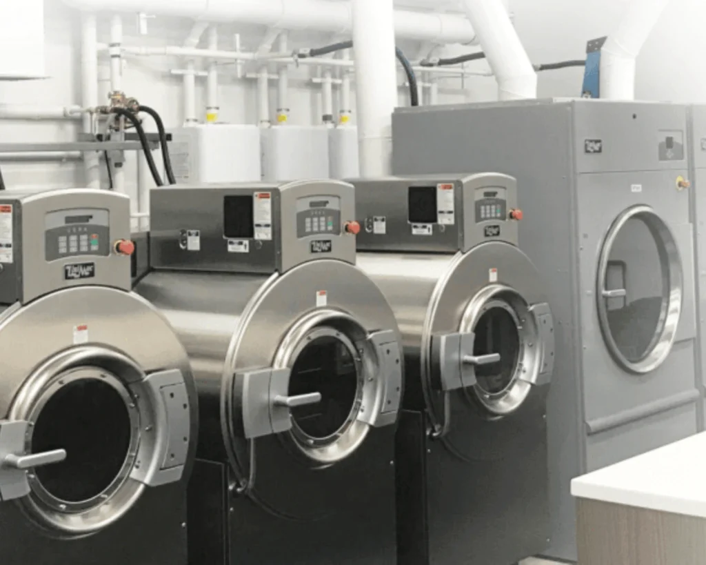 Row of commercial washers in an on-premise laundry room where operators may need to schedule laundry equipment service