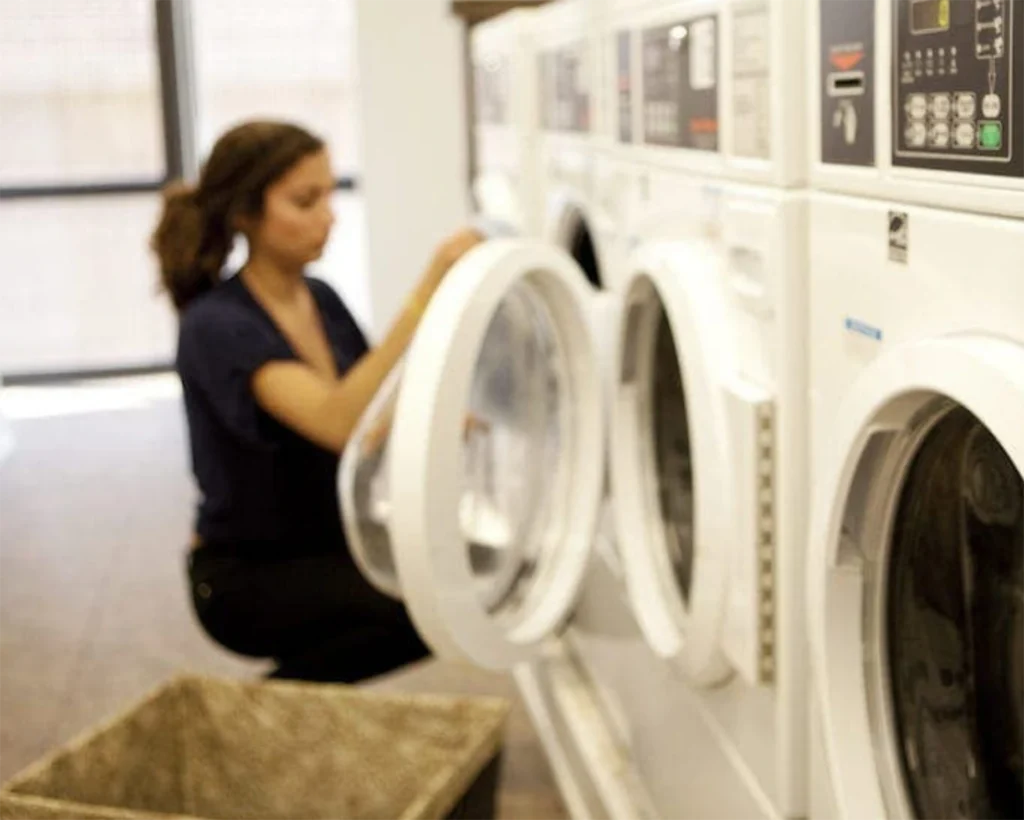 Resident using commercial washer and dryer equipment in a shared apartment laundry room supported by SELaundry in Rincon.