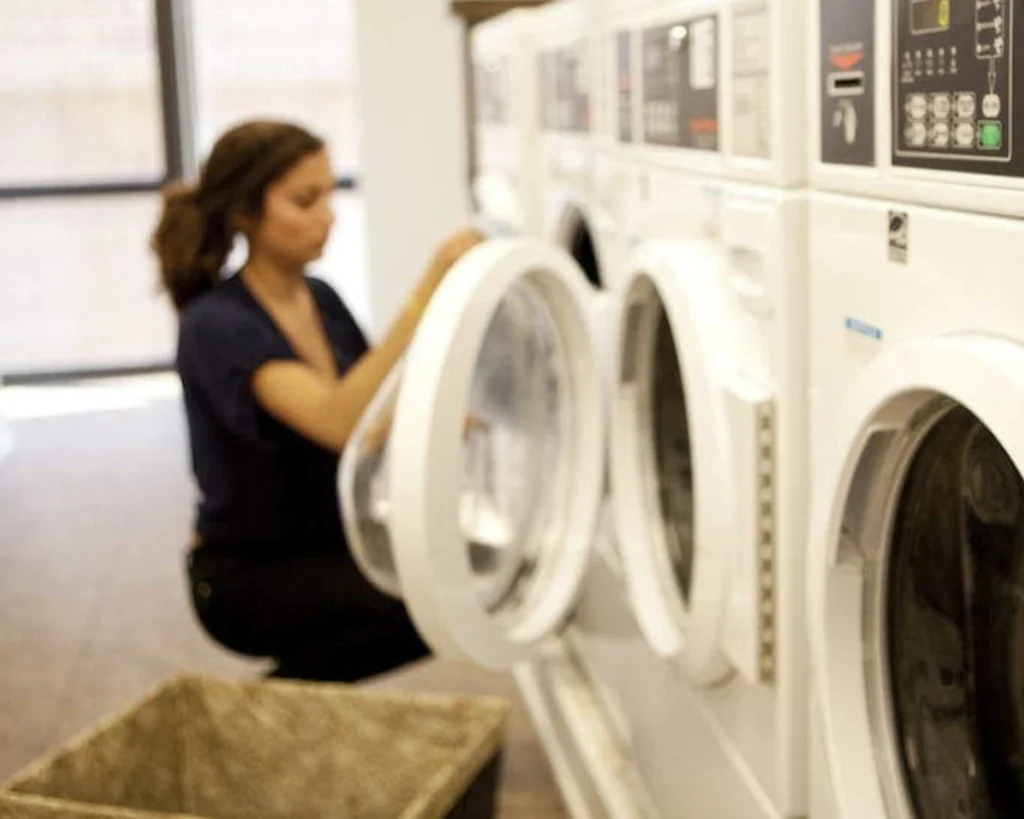 Customer loading laundry into a front-load washer inside a bright and clean self-service laundromat.