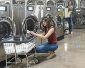 Customer loading laundry into a Huebsch commercial washer inside a modern self-service laundromat.