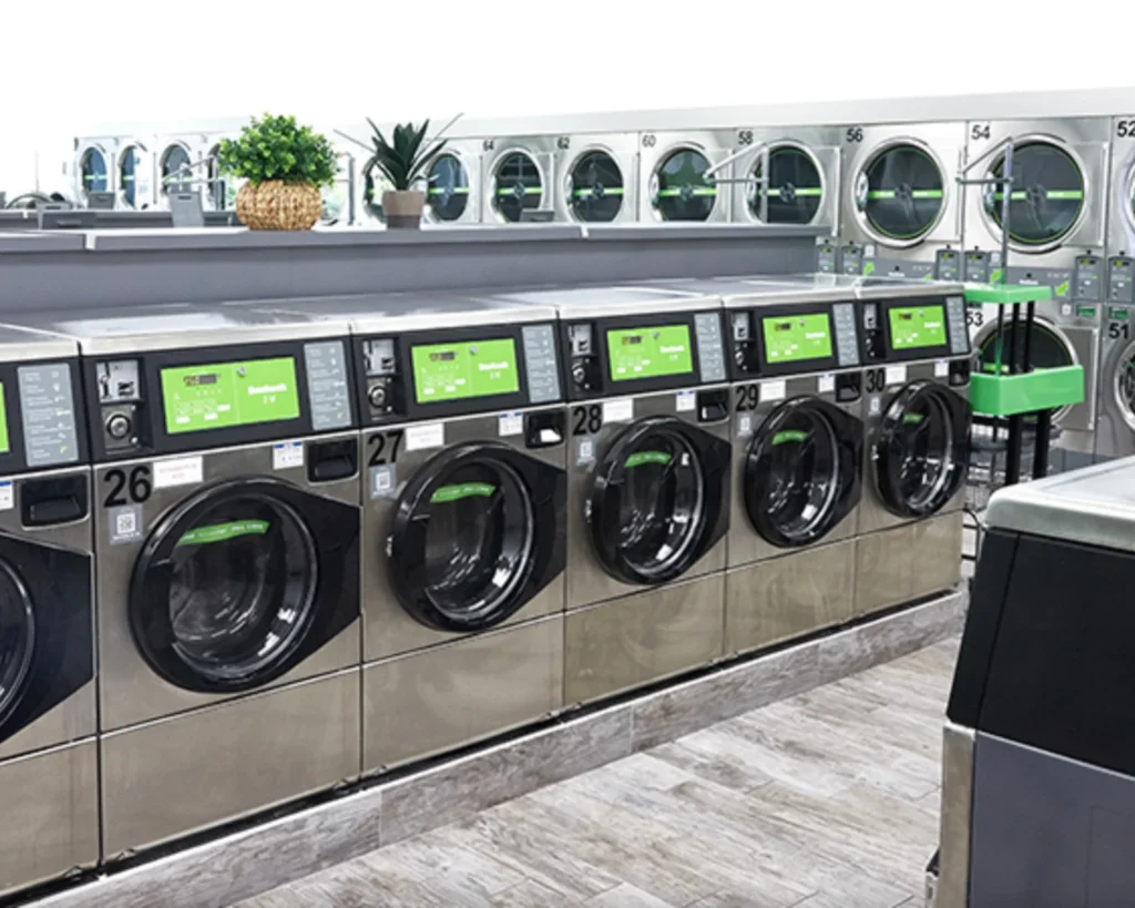 Row of Huebsch commercial washers with digital controls in a clean and organized laundromat.