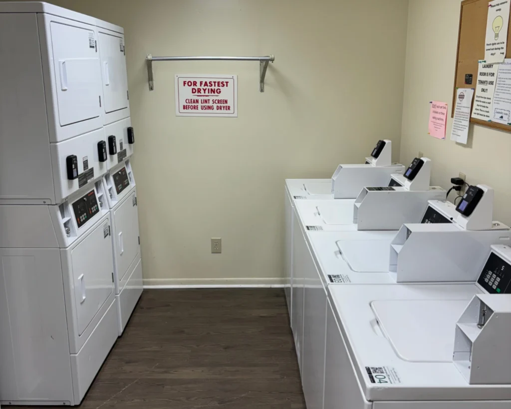 Multi-housing laundry equipment installed in an apartment laundry room with washers and stacked dryers