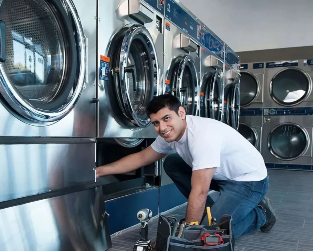 New laundromat owner planning commercial laundry equipment maintenance with a technician servicing a laundromat machine.
