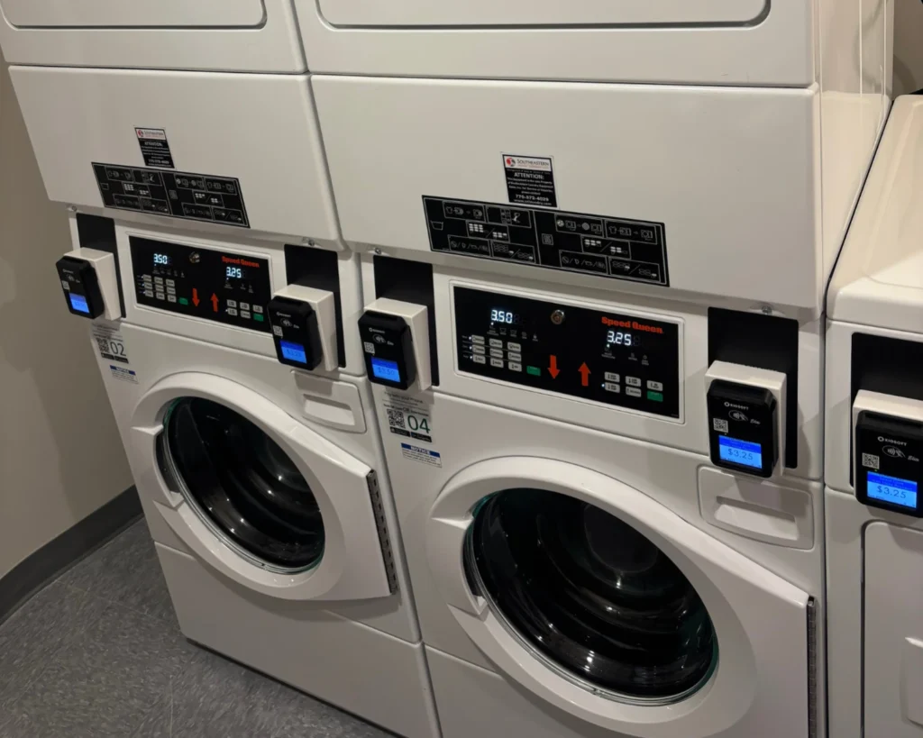 Stacked commercial washers and dryers with payment readers that help prevent laundromat equipment damage.