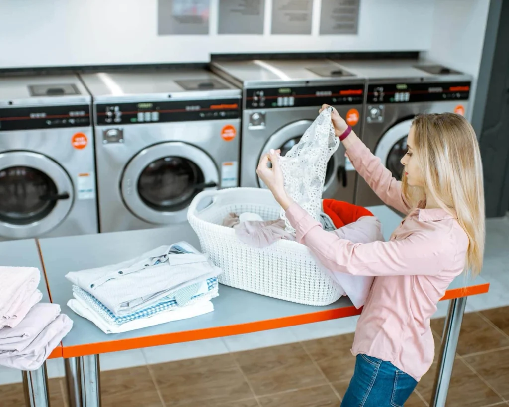 Laundry equipment for multifamily student housing with a woman folding clothes at a shared laundry room table.
