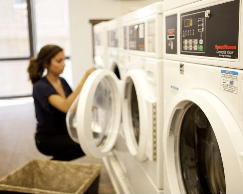Laundry equipment for multifamily student housing with Speed Queen front-load washers and a woman loading a machine.